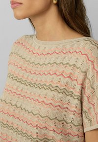 Beige gebreide top met een zigzagpatroon in roze en groene tinten, met een ronde halslijn en korte mouwen, en een gestructureerd ontwerp.