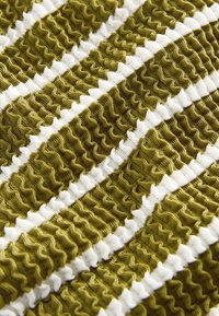 Tessuto verde oliva testurizzato con strisce bianche ondulate; presenta sezioni arricciate che creano un effetto increspato in tutto il tessuto.