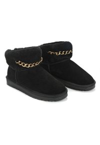 Schwarze Wildleder-Stiefeletten mit einem Kunstfellbund und einem goldenen Kettenakzent entlang der Oberseite. Gummisohlen mit strukturiertem Grip.