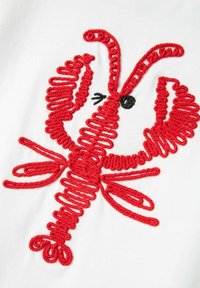 Diseño de langosta bordado en rojo sobre un fondo de tela blanca, que presenta texturas y curvas detalladas del cuerpo y las pinzas de la langosta.