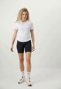 Mujer rubia caminando hacia adelante, vestida con una camiseta blanca de Nike, pantalones cortos de ciclista negros, calcetines blancos de Nike y zapatillas de correr blancas con acentos naranjas.