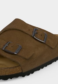 Καφέ σουέντ σανδάλι Birkenstock με δύο ρυθμιζόμενες μεταλλικές αγκράφες και διαμορφωμένο φελλό πάτο με μαύρη σόλα.