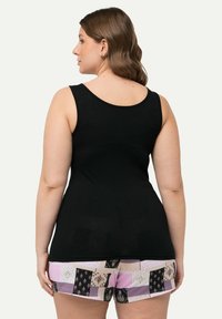 Schwarzes Tanktop mit breiten Trägern, kombiniert mit gemusterten Shorts, die Patches in Pink, Beige und Schwarz aufweisen. Glatte, weiche Textur.