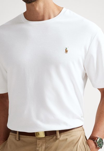 Vit bomullst-shirt med rund halsringning och korta ärmar, med en liten broderad logotyp av en häst och ryttare på vänster bröst.