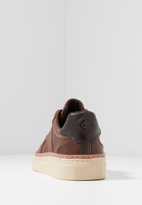 Brune lædersneakers med en tekstureret overflade, kontrasterende mørkebrun detaljer, høj ryg og en gummisål med et mønstret greb.