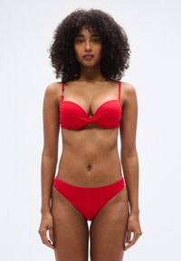Κόκκινο μπικίνι με στριφτό μπροστινό σχέδιο, λεπτές τιράντες και χρυσές μεταλλικές λεπτομέρειες. Λεία υφή και εφαρμοστή γραμμή, παρέχοντας μέτρια κάλυψη.