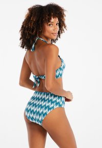 Teal ja valgenüanssidega zigzag-mustri bikinitopp, millel on kaeluse ja selja sidumiseks nöörid; kõrge vöökohaga aluspüksid.