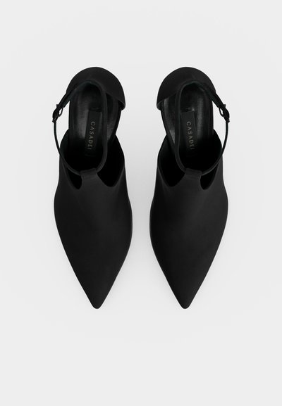 Paire de chaussures noires à bout pointu avec brides à la cheville, vues de dessus sur un fond blanc.