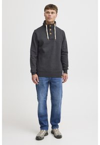 Pulover gri închis cu guler înalt, nasturi din lemn și șnururi de ajustare. Asortat cu blugi albastru deschis și încălțăminte sport.