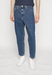 Mörkblå denimjeans med avslappnad passform och insvängd ankel, med fem fickor och medelhög midja. Matcher med vita sneakers.
