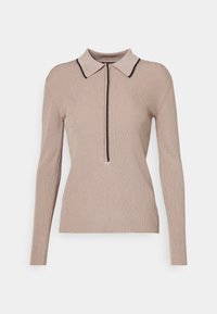 Beige ribbet striktrøje med lange ærmer, kraveudskæring, halv lynlås fortil og kontrasterende mørk kant langs kraven og lynlåsen.