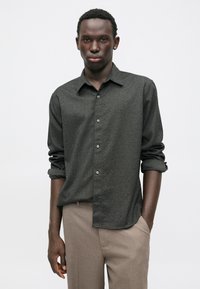 Ciemnoszara koszula z guzikami, o fakturowanym wzorze, z zawiniętymi rękawami i srebrnymi guzikami, w zestawieniu z jasnobrązowymi spodniami.