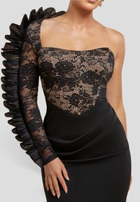 Sort blondekjole med en struktureret overdel med blomsterprint, ét blonderærme og et glat satin nederdel med drapering.