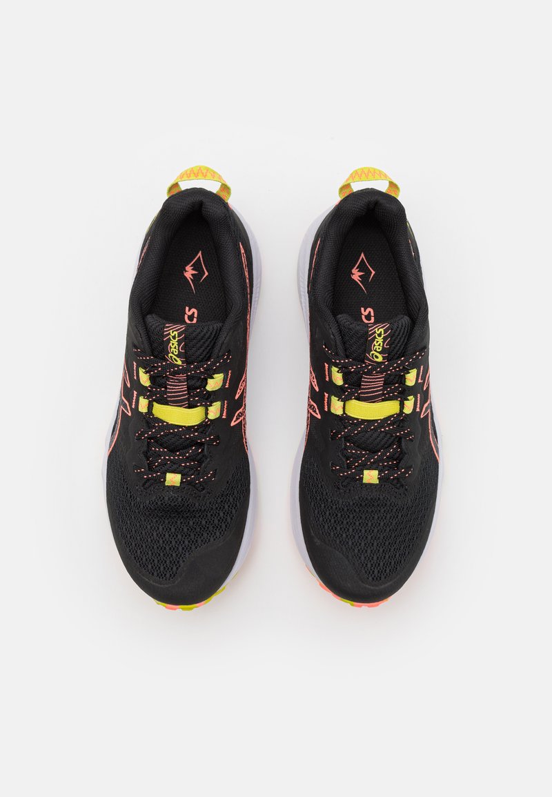 Zapatos deportivos negros con parte superior de malla, acentos rosas vibrantes, cordones amarillos y suelas blancas. Presentan un collar acolchado y una superficie texturizada.