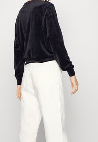 Svart sammet långärmad topp med rundad halsringning, tillsammans med vita vida byxor med hög midja och bakfickor.