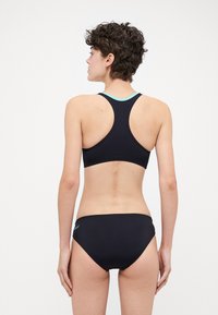 Černý dvoudílný bikini s topem na sportovce a světle modrým lemováním a odpovídajícími nízkými kalhotkami, oba vyrobené z hladké a elastické tkaniny.