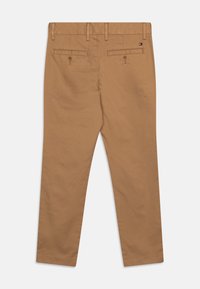 Chino color khaki con una texture liscia, taglio dritto e due tasche posteriori con chiusure a bottone. Dettaglio del marchio discreto sulla cintura.