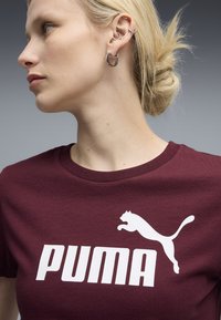 Bordo pamučna majica s velikim bijelim logom "PUMA" i grafikom skakačkog pumaa. Majica ima okrugli izrez i kratke rukave.
