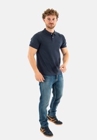 Camisa polo navy de mangas cortas y cuello, combinada con jeans desgastados de color azul claro y zapatillas negras con detalles en marrón.