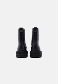 Paire de bottines en cuir noir vues de derrière, avec des languettes de tirage et des semelles épaisses à plateforme sur un fond blanc.