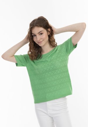 Groen, kort mouwenshirt met een gebreide textuur in een patroon met zigzagontwerpen. Gecombineerd met witte broek, met een ontspannen pasvorm.