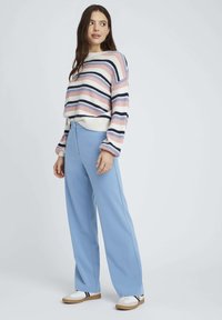 Pull en tricot rayé dans les tons rose, bleu et marine avec une coupe ample ; associé à un pantalon large taille haute bleu clair ; baskets blanches.