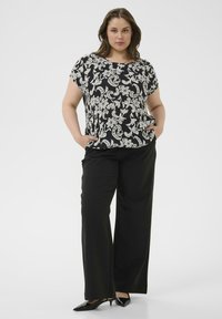 Zwart-wit top met bloemenpatroon en korte mouwen, gecombineerd met zwarte broek met wijde pijpen en zwarte schoenen met puntige neus. Glad stofoppervlak.