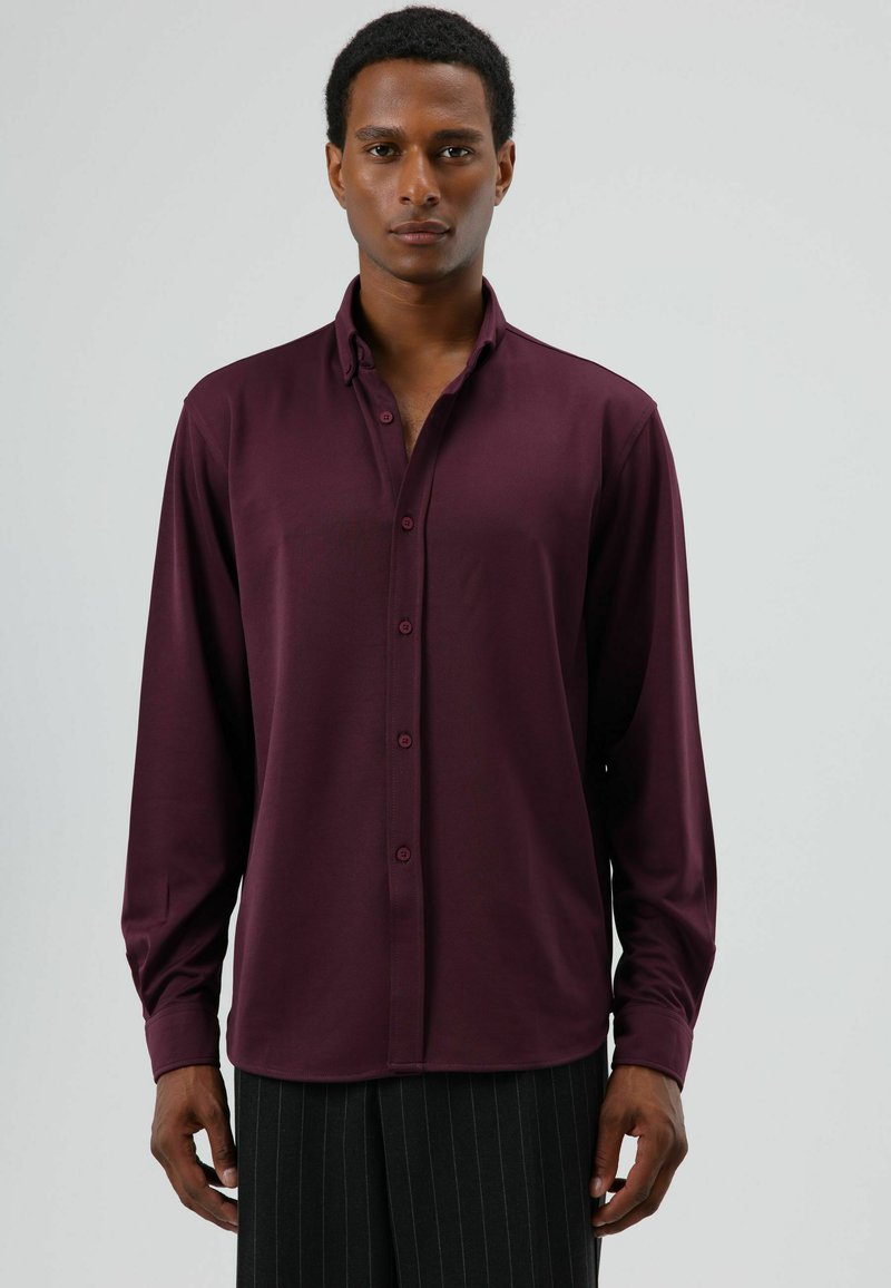 Langarmshirt in diep bordeauxrood, gemaakt van gladde stof met knopen aan de voorkant en een puntige kraag, gecombineerd met fijn gestreepte broek.