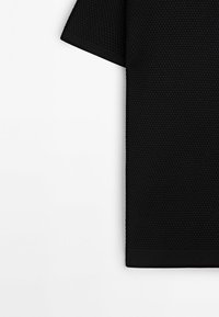 Top court en tricot noir à manches courtes présentant un motif texturé, un col rond et des bords côtelés aux manches et à l'ourlet.