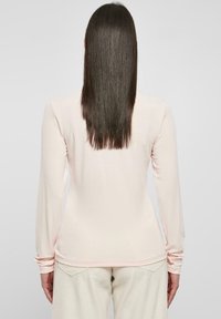 Hellrosa Langarmshirt mit schlanker Passform, rundem Ausschnitt und feiner gerippter Textur. Die Rückseite hat ein glattes Design ohne Verzierungen.