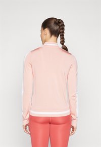 Rózsaszín, könnyű pulóver hosszú ujjal, fehér díszítéssel az oldalán, bordázott gallérral és aljjal. Korall színű leggings felett viselve.