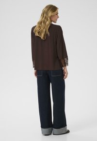 Brown blouse with lace trim at sleeves, paired with wide-leg dark denim jeans featuring a cuffed hem and contrasting inner fabric.