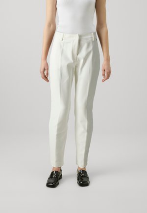 Pantaloni bianchi su misura con una vestibilità slim, dotati di fronte piatto, passanti per cintura e una texture liscia. Abbinati a mocassini neri.