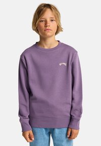 Sweat-shirt violet à col rond, bord-côtes aux poignets et à l'ourlet. Présente le logo "Billabong" de couleur claire sur la poitrine. Associé à un jean bleu clair.