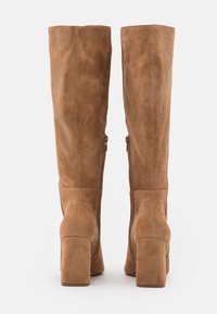Bottes montantes en daim marron avec un talon bloc, dotées de fermetures éclair latérales et d'un design épuré et épuré. Texture douce avec des accents minimalistes.