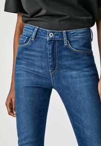 Blå denim högmidjade jeans med slim fit, framfickor och kontrasterande sömmar. Knäppning med knapp och bältesloopar.