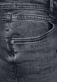 Jeans de mezclilla oscura con un acabado texturizado, que cuentan con un pequeño botón de metal cerca del bolsillo trasero y un pespunte de contraste a lo largo de las costuras.