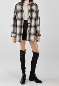 Kostkovaná košile v krémové a černé barvě s knoflíkovou légou a dvěma náprsními kapsami. Kombinována s žebrovaným svetrem s vysokým límcem a černou mini sukní. Černé kozačky nad kolena.