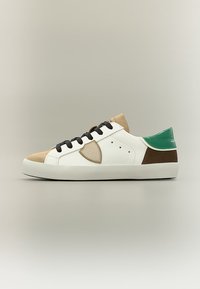 Baskets basses avec côtés en cuir blanc, bout et languette en daim beige, lacets noirs, talon marron, languette de talon verte et écusson latéral beige.