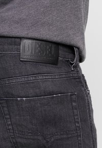 Černé džíny z denimu s texturovanou koženou nášivkou označenou "DIESEL" přišitou na zadním pase, s prošívanými kapsami a vybledlým vzhledem.