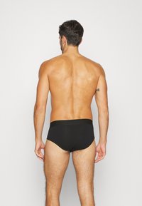 Schwarze Baumwollslips mit breitem elastischen Bund, von hinten betrachtet, die eine glatte Textur und eine figurbetonte Passform zeigen.