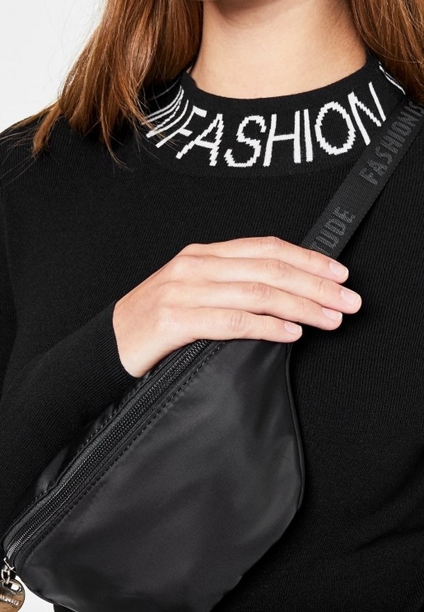Svart nylonmidjeväska med ett dragkedjeförsett fack, bärs tvärs över kroppen. Har en texturerad rem med ordet "FASHION" i kontrasterande vitt.
