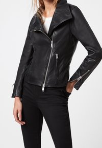 Svart lädermotorcykeljacka med en bred krage, asymmetrisk framdragkedja och dragkedjefickor på sidorna, med silverfärgade detaljer.