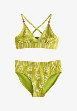 Két részes fürdőruha élénk zöld színben, fehér virágmintákkal. A felső rész keresztbe futó pántokkal és szegélyezett aljjal rendelkezik, míg az alsó rész derékpántos kiemelést tartalmaz.