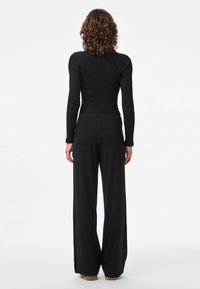 Czarny prążkowany top z długim rękawem w połączeniu z szerokimi czarnymi spodniami. Strój charakteryzuje się dopasowanym krojem i miękką teksturą oraz prostą sylwetką.