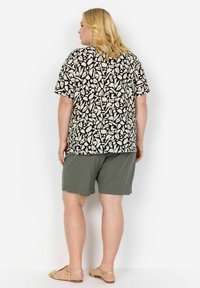 Korte mouwen zwart-wit patroon top met beige accenten, gecombineerd met olijfgroene shorts. Sandalen hebben een gevlochten detail.