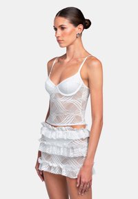 Top corto in pizzo bianco con spalline sottili e un design a fantasia, abbinato a una mini gonna a balze con strati realizzata nello stesso materiale in pizzo.