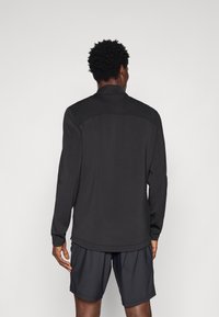 Svart långärmad topp med ståkrage, som har en slät textur och en något avsmalnande design, ihop med mörka shorts.