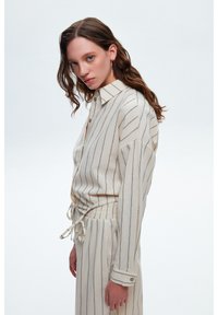 Set di camicia e pantaloni a righe beige, con collo a camicia, chiusura con bottoni, maniche lunghe, vita con cordino e tessuto leggero.