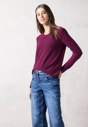 Bordeaux kleurige trui met lange mouwen en ribbelstructuur, gecombineerd met lichtblauwe relax-fit jeans met zijzakken en een vervaagde afwerking.